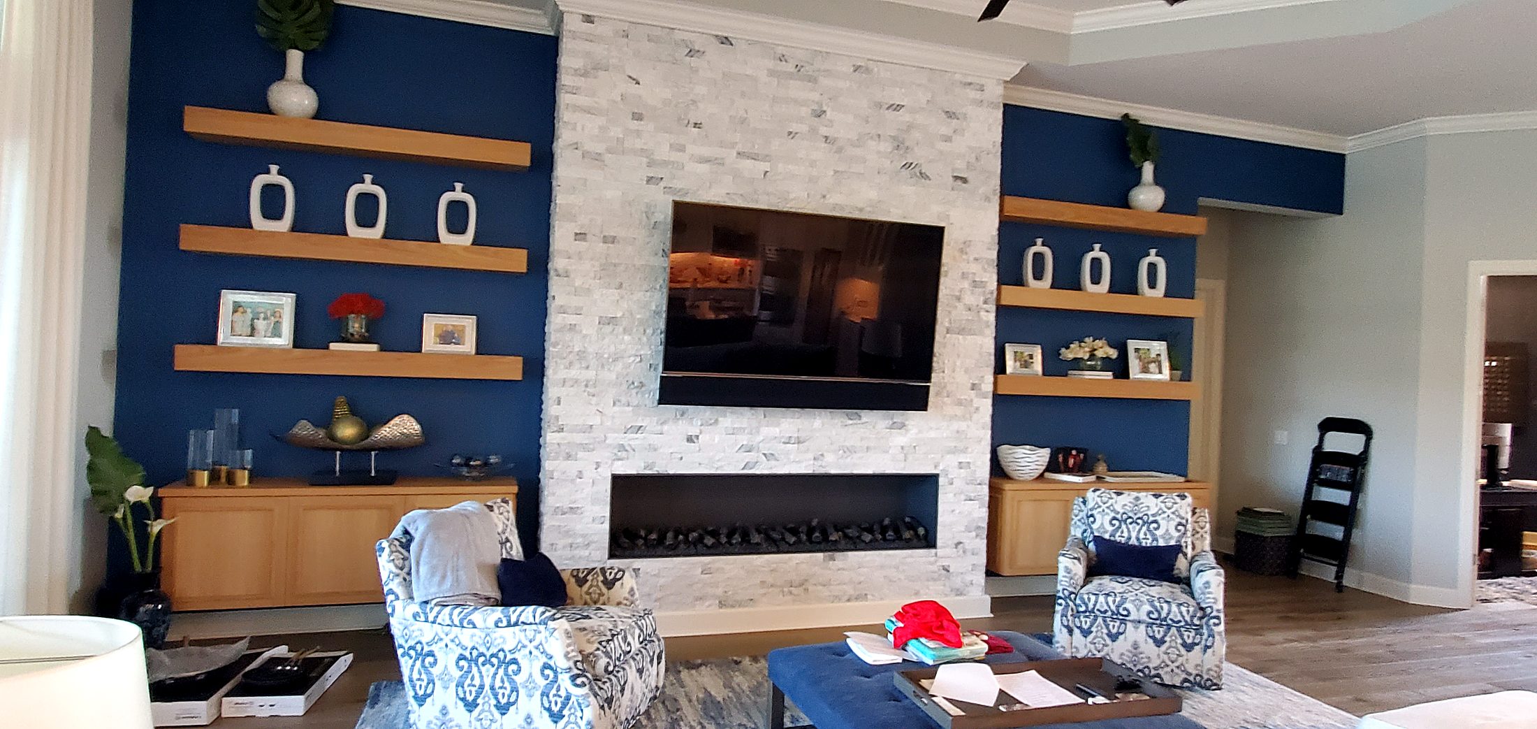 Navy living room with oak floating shelves and stone fireplace